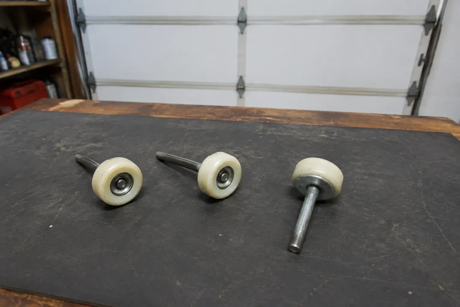 Three detached nylon-wheel garage door rollers with steel stems on a work mat. — Garage Door Roller Replacement, Oakville