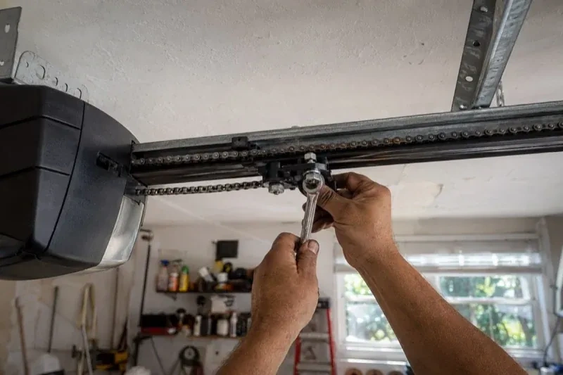 Hands holding a wrench against an opener trolley beneath a chain rail — Chain-Drive Opener Repair, Oakville