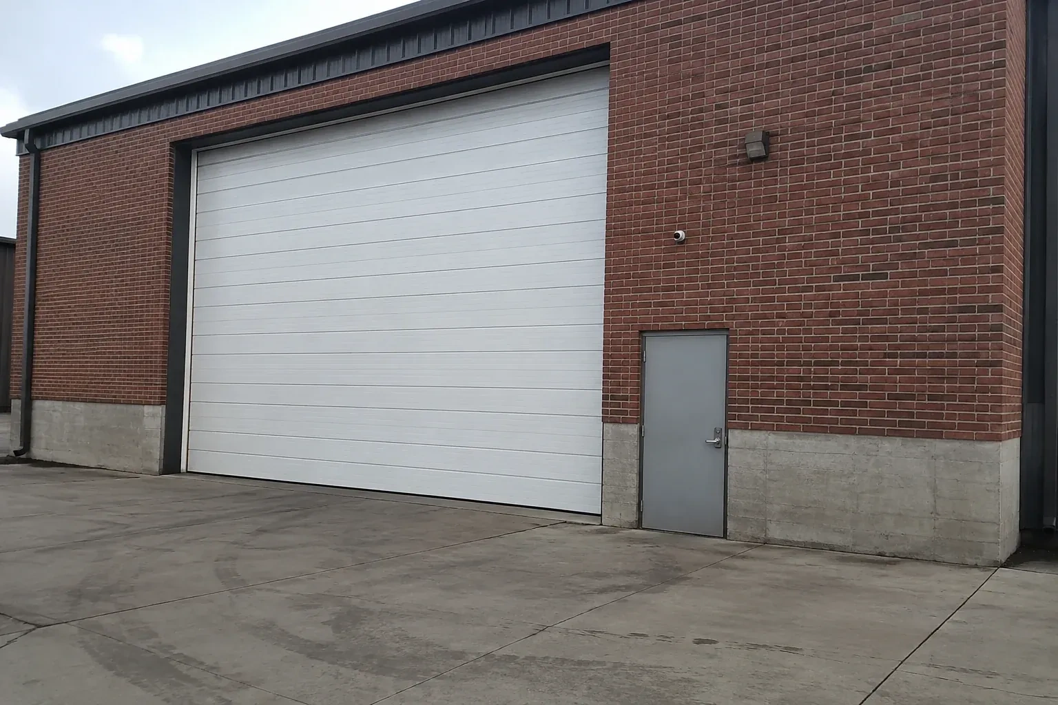 Tall closed sectional loading door beside a personnel door at a brick unit. — Commercial Sectional Door Repair, Oakville