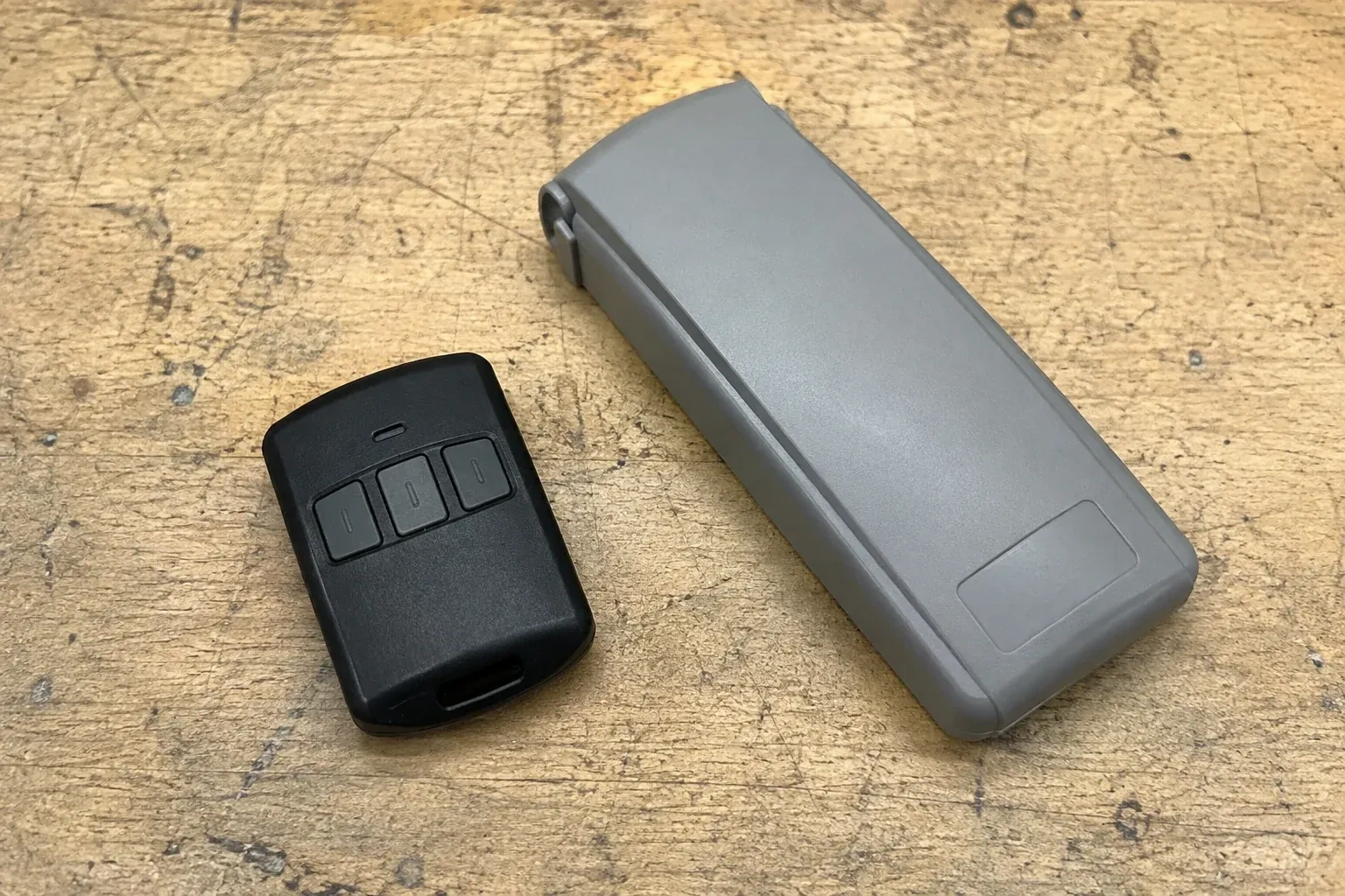 Three-button remote beside a closed grey keypad cover on a workbench. — Garage Door Remote and Keypad Programming, Oakville